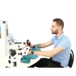 Man in a light blue polo seated at a white lab desk using diagnostic equipment and a cuff on the desk nearby