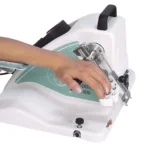 Close-up of a hand operating a compact handheld device with metal clamps on a white base.