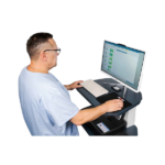 Healthcare professional in light blue scrubs using a computer workstation to review patient data.