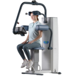Woman seated in a VR-assisted rehabilitation machine, wearing a headset and using the padded supports for a guided seated workout.